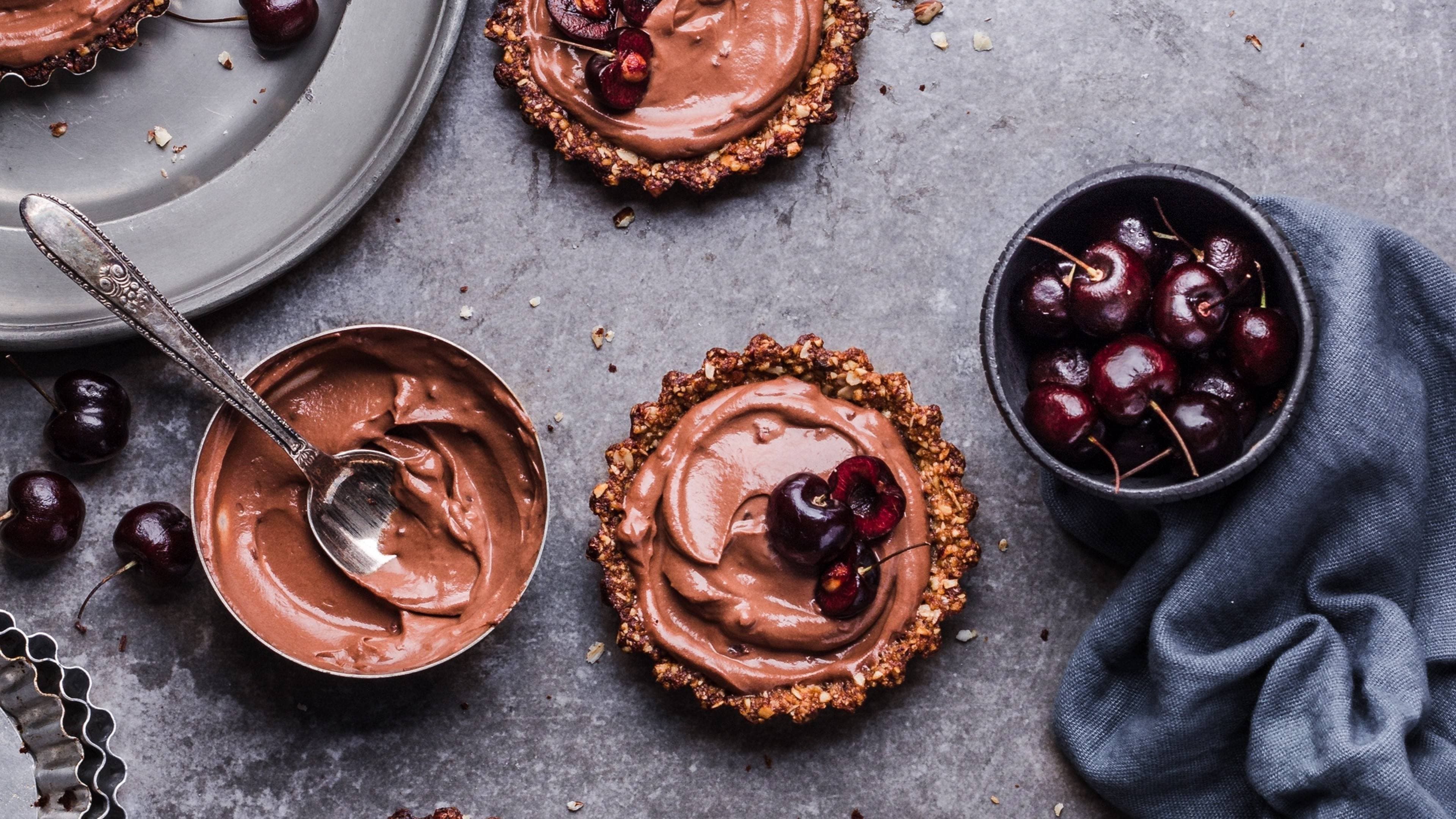 Chocolate cherry tarts with ganache filling beside fresh cherries and a bowl of mousse